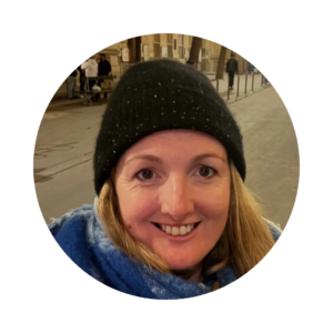 Smiling person wearing a black knit hat and blue scarf, photographed outdoors at night on a city street.